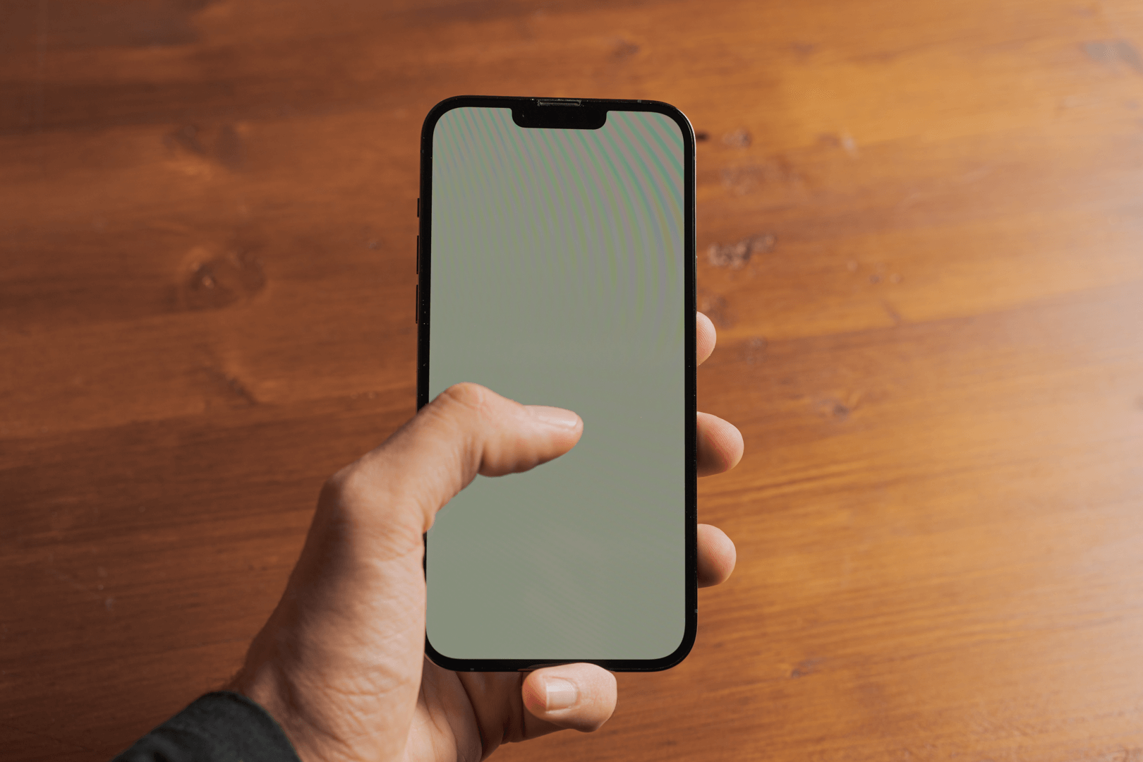 Mano sosteniendo un teléfono móvil sobre una mesa de madera