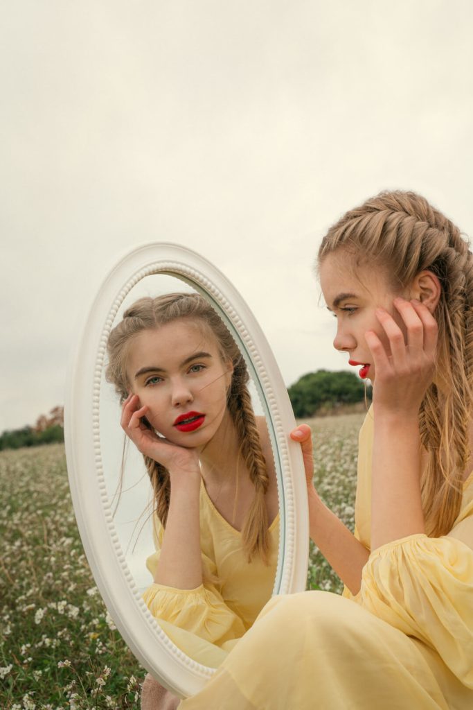 Chica con vestido amarillo reflejada en un espejo en medio del campo