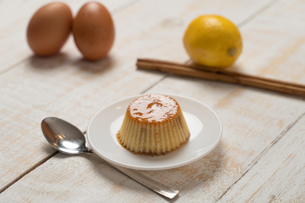Flan casero en un plato junto a huevos, limón y una rama de canela