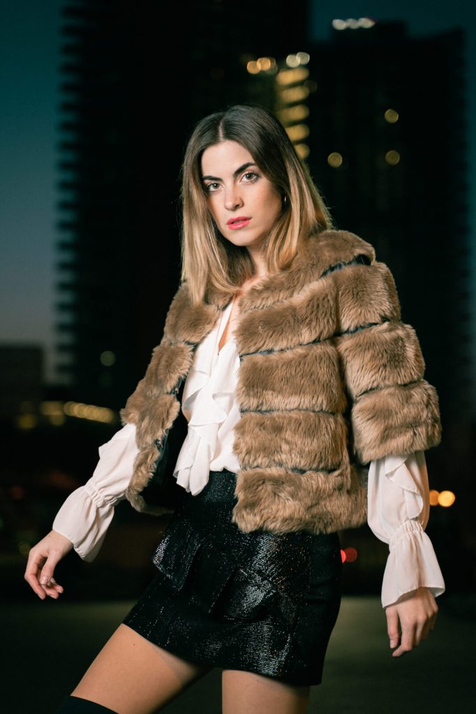 Sesión de moda nocturna: mujer con chaqueta de pelo marrón y falda negra en la ciudad