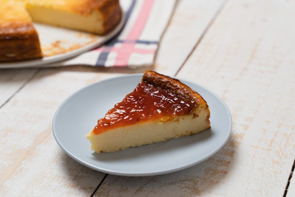 Porción de tarta de queso con mermelada en un plato sobre mesa blanca