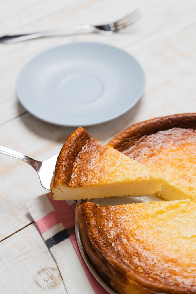 Porción de tarta de queso levantada con una pala junto a un plato vacío