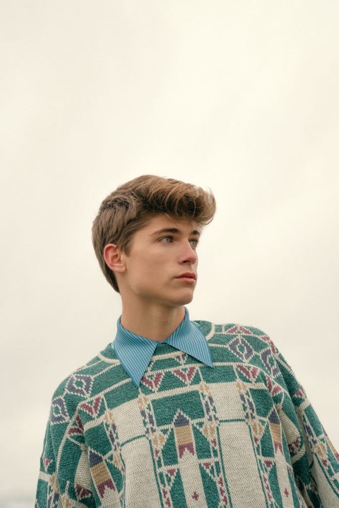 Retrato editorial de un chico con camisa de cuadros verdes sobre cielo claro