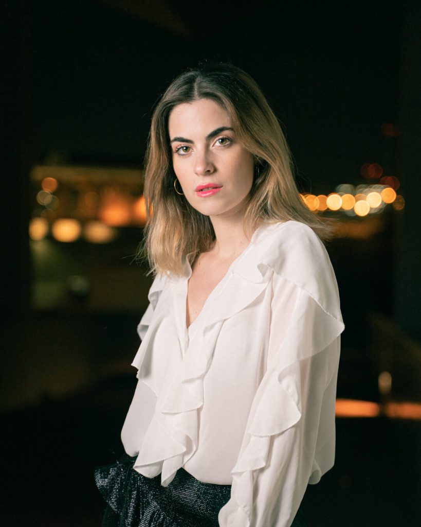 Retrato nocturno de una mujer con blusa blanca y luces desenfocadas de fondo
