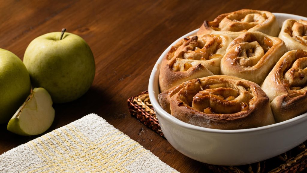 Primer plano de rollos de canela en una fuente blanca con manzanas verdes, fotografía para carta de restaurante