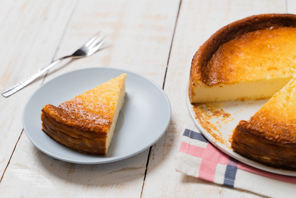 Tarta de queso entera junto a una porción servida en un plato