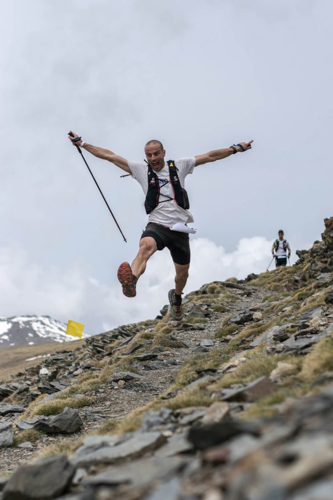 Corredor de trail con los brazos abiertos en una ladera rocosa, fotografía deportiva